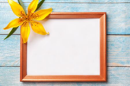 Brown wooden photo frame with yellow flowers lily on old blue shabby background with copy space. Floral greeting card, flat lay.の写真素材