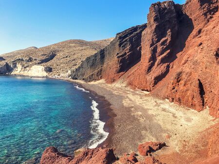 Red volcanic beach in Santorini, Greece. The azure water of the Mediterranean Sea in the bay off the...