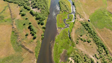 Wide calm river surrounded by green meadows and trees near brown ground road with travel driving...