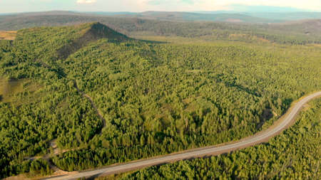 Aerial panoramic view from drone of forests, rural road and hills. Shot of countryside landscape and nature on sunset. Empty road and highway, birds eye view. Open space.の写真素材