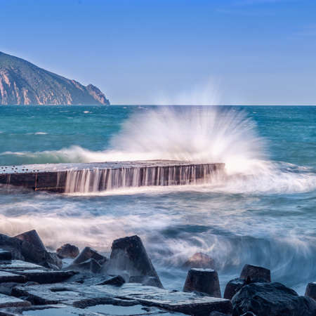 Rocky sea shore in sunny day. Waves crash against about breakwaters and pier. Beautiful nature seascape in summer.の写真素材