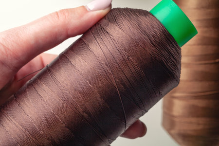 Female hand holding green skein and bobbin of brown thread for sewing, closeup. Materials for...