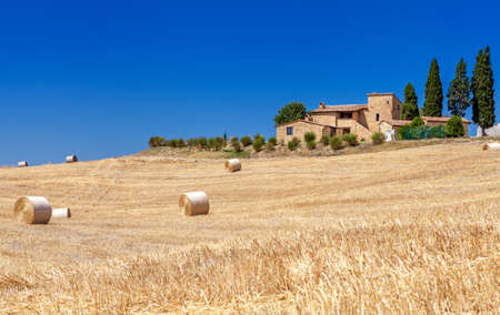 Rural landscapes of Tuscany, Italy. Lots of round bales and haystacks in the fields. Brick farmhouse standing on a hill among the pitch.の写真素材