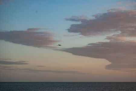 The soft colorful sky of a sky with clouds over a sea and the horizon at sunrise or sunset and a pelican flying over the ocean.の写真素材