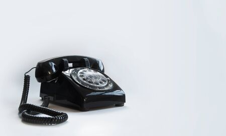A retro black rotary telephone with a cord against a white backgroundの写真素材