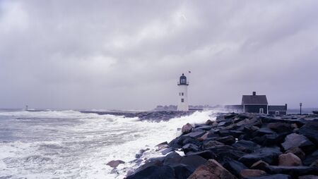 Scituate lighthouse in Massachusetts stands against a nor easter, with waves crashing against the breakwater.の写真素材