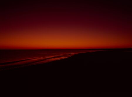 Scary red and orange horizon with the ground and waves in silhouette.