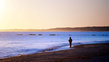 A fisherman at sunrise on a cape cod beach with a calm ocean.の写真素材