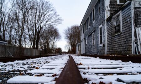 Brown track and leaves covered in snow and beside a broken down house.の写真素材