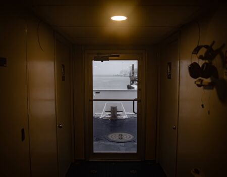 A hallway with bathrooms and a door in a commuter ferry on a gloomy day.