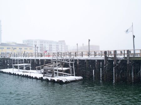 Snow covers a dock and buildings and water in a marina.の写真素材