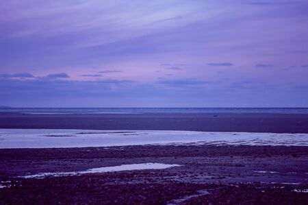 Beautiful landscape with a rocky beach and water and a soft purple sky.の写真素材