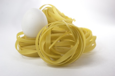 Italian pasta tagliatelle nest and egg isolated on white backgroundの写真素材