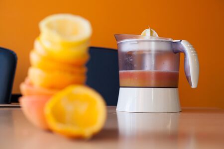 Electric juicer full of fresh citrus juice with a pile of squeezed citruses out of focusの写真素材