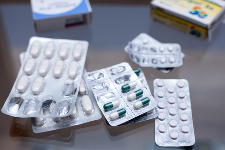 Various pills and capsules in blister packagings laid out on a glass tableの写真素材