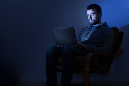 Young man working on a laptop in a dark room at nightの写真素材