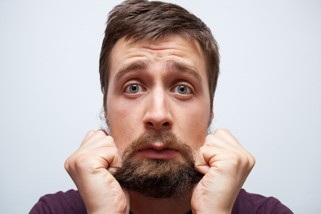 Young bearded man pulling at his long messy beard in frustration and stressの写真素材