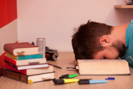 Student passed out tired in the middle of a large book while studyingの写真素材