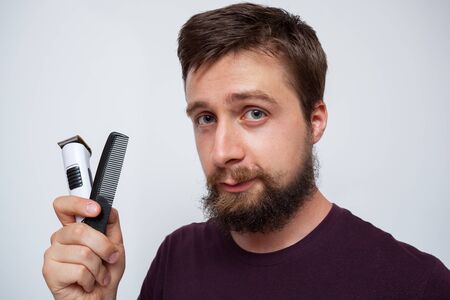 Young bearded man holding up an electrical trimmer and combの写真素材