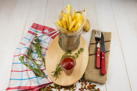 french fries in a metal basket on a wooden background with seasonings