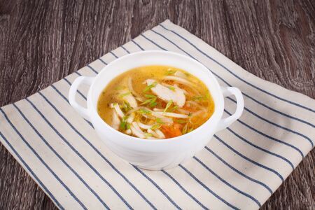Chicken soup on a wooden background with a linen towel in a white tureenの写真素材