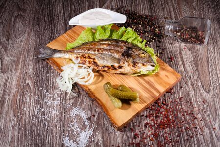Grilled sea bream on a wooden board and lettuce, tartar sauce with pickles. The concept of grill, barbecue.の写真素材