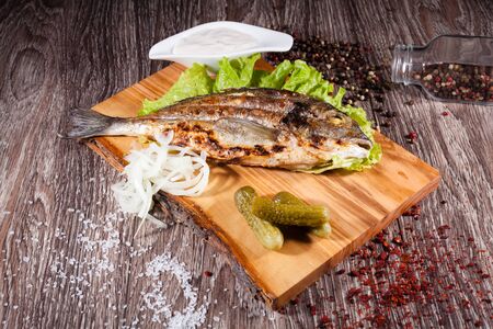 Grilled sea bream on a wooden board and lettuce, tartar sauce with pickles. The concept of grill, barbecue.の写真素材