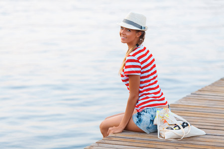 Young beautiful happy woman sitting on the pierの写真素材