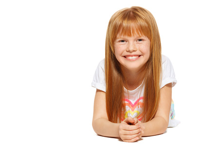 A cheerful little girl with red hair is lying; isolated on the white backgroundの写真素材