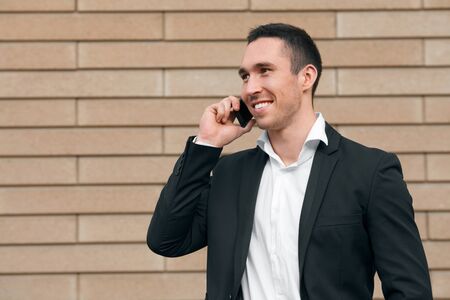 Smiling happy man talking on mobile phone in a black suit, happy modern man. Outdoorsの写真素材