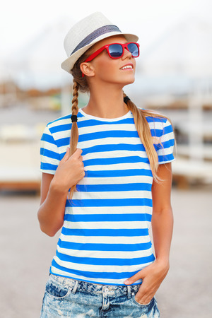 Beautiful sexy girl in sunglasses, in shorts and striped t-shirt, in hat, outdoors. Tanned woman in summerの写真素材