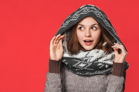 Surprised christmas girl wearing knitted wear scarf. Excited  beautiful smiling girl, winter concept, isolated over red backgroundの写真素材