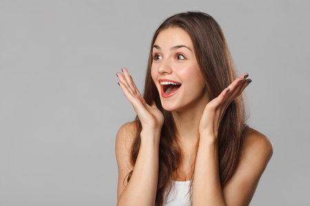 Surprised happy beautiful woman looking sideways in excitement. Isolated on gray backgroundの写真素材