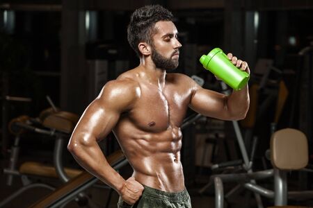 Sexy muscular man drinking water in gym, shaped abdominal. Strong male naked torso abs, working outの写真素材