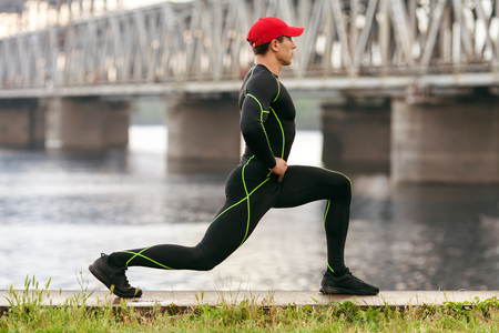 Athletic man doing stretching exercises, outdoor. Active male working out outside on the background of the bridgeの写真素材
