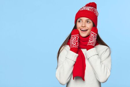 Surprised happy woman looking sideways in excitement. Christmas girl wearing knitted warm hat and scarf, isolated on blue backgroundの写真素材