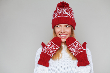 Surprised happy beautiful woman looking sideways in excitement. Christmas girl wearing knitted warm hat and mittens, isolated on gray backgroundの写真素材