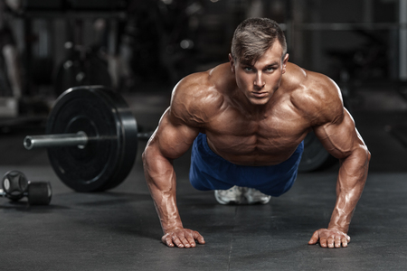 Muscular man working out in gym doing push-ups exercises, strong male naked torso absの写真素材