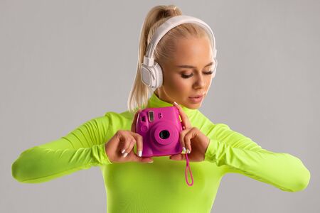 Beautiful girl with a camera, fashion woman photographer in colored clothes, isolated on the gray backgroundの写真素材