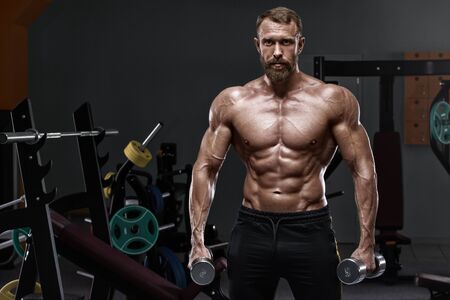 Muscular man in gym with dumbbells. Strong male naked torso abs, workoutの写真素材