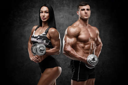 Sporty couple working out with dumbbells on wall background. Muscular man and womanの写真素材