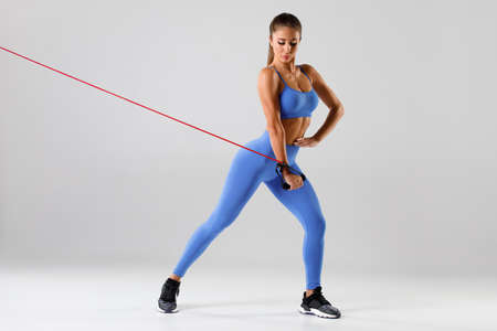 Fitness woman exercise with resistance band on gray background. Athletic girl working outの写真素材