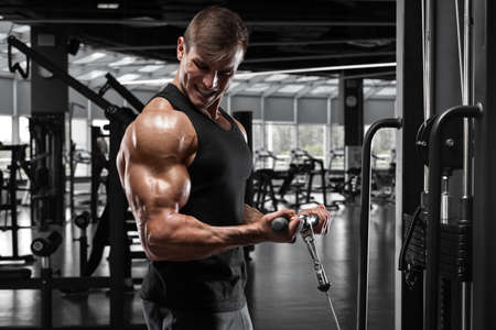 Muscular man working out in gym doing exercise for biceps, strong male bodybuilder