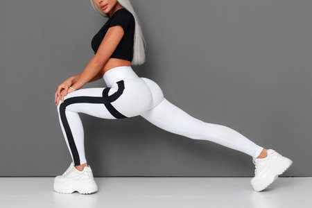 Fitness woman doing lunges exercises for leg muscle workout training. Active girl doing front forward one leg step lunge exercise, on gray backgroundの写真素材