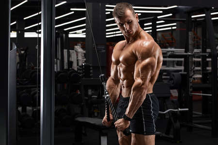 Muscular man in gym doing exercises for triceps, working out. Strong male naked torso abs