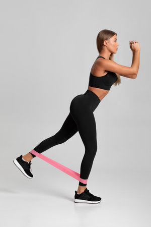 Fitness woman doing exercise for glutes with resistance band on gray background. Athletic girl working outの写真素材