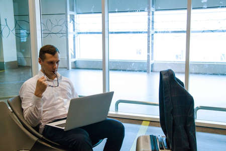 Portrait of handsome young man working with laptop in airport when waiting for his plane.