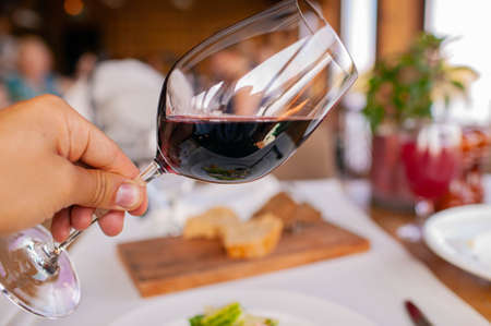 image of man's hand holding red wine from glassware in restaurantの写真素材