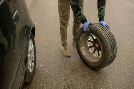 The driver changes the wheel of the car. Change summer wheels for winter.