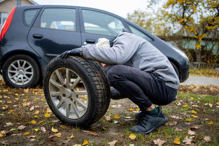 The driver changes the wheel of the car. Change summer wheels for winter.